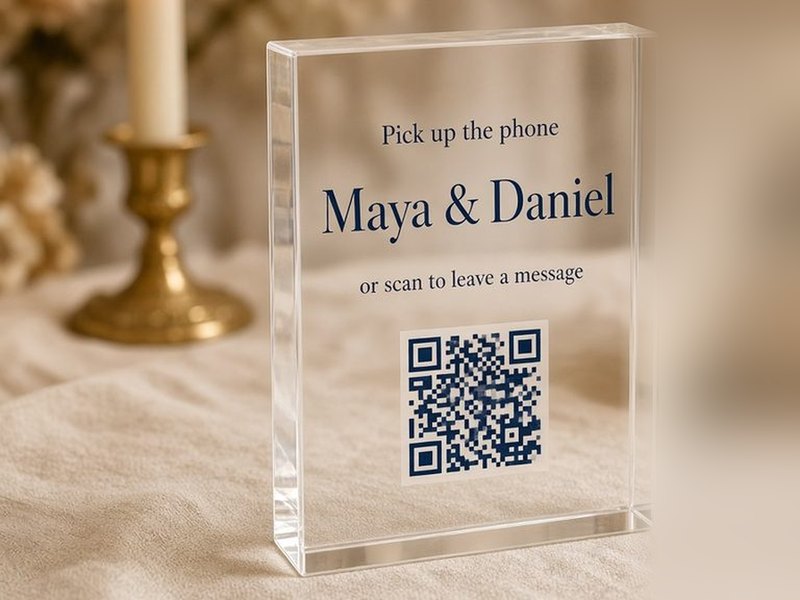 The acrylic table sign with the couple’s names and QR code, beside a candle